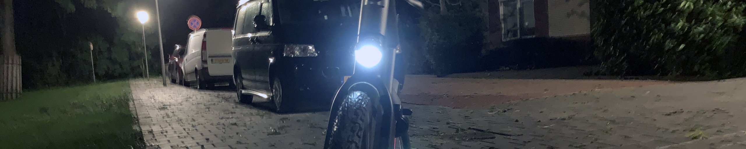 Een fiets met voorlicht aan in het donker, op de grond is nog de reflectie van het rode achterlicht te zien